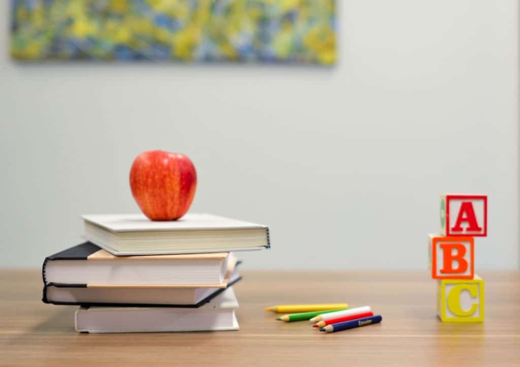 An apple balances on a stack of book beside colored pencils and alphabet blocks, hinting to the educational nature of this blog post.