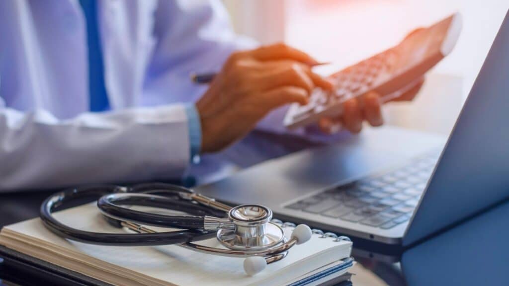 Doctor working on calculator and computer with stethoscope close at hand