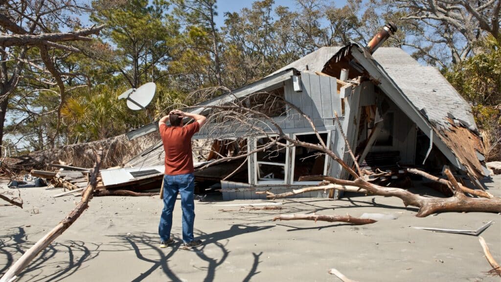 Man in distress stands in front of home destroyed by a storm.