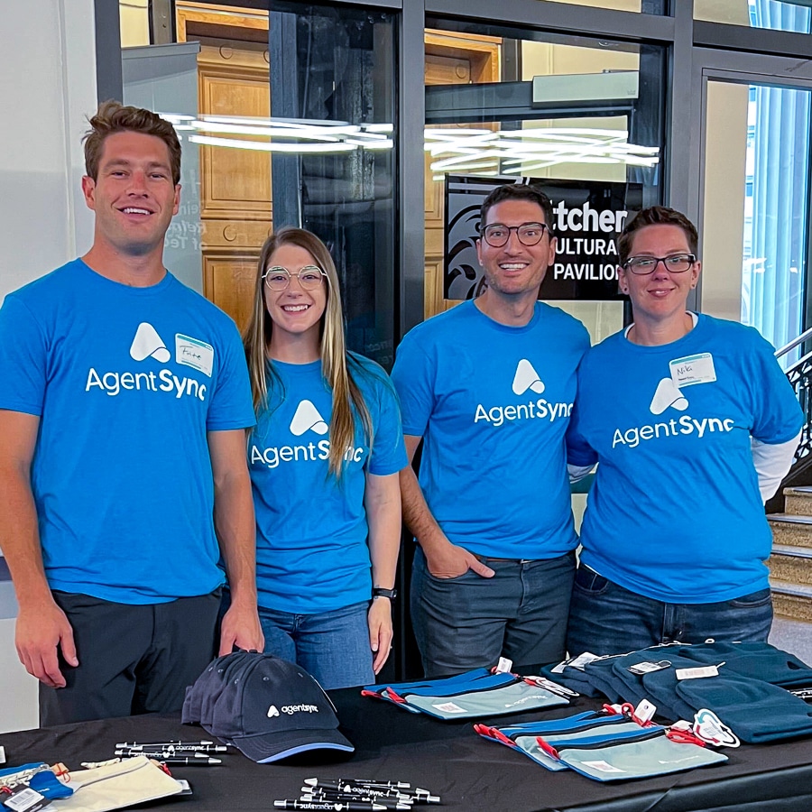 Four AgentSync employees in matching blue shirts pose together at the Denver Startup Week job fair.