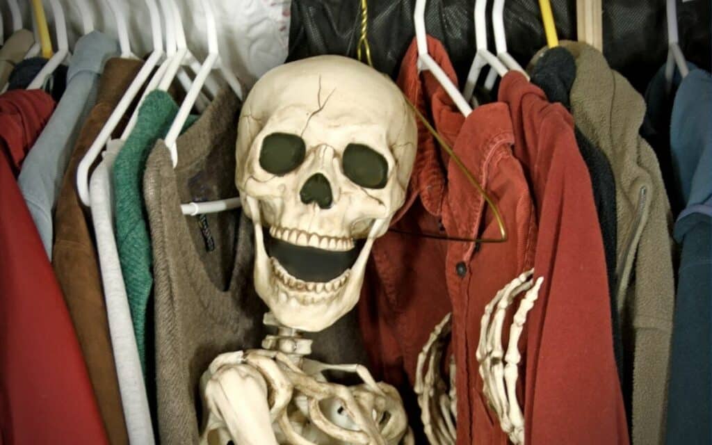 Skeleton peeking out from clothes hanging in a closet.